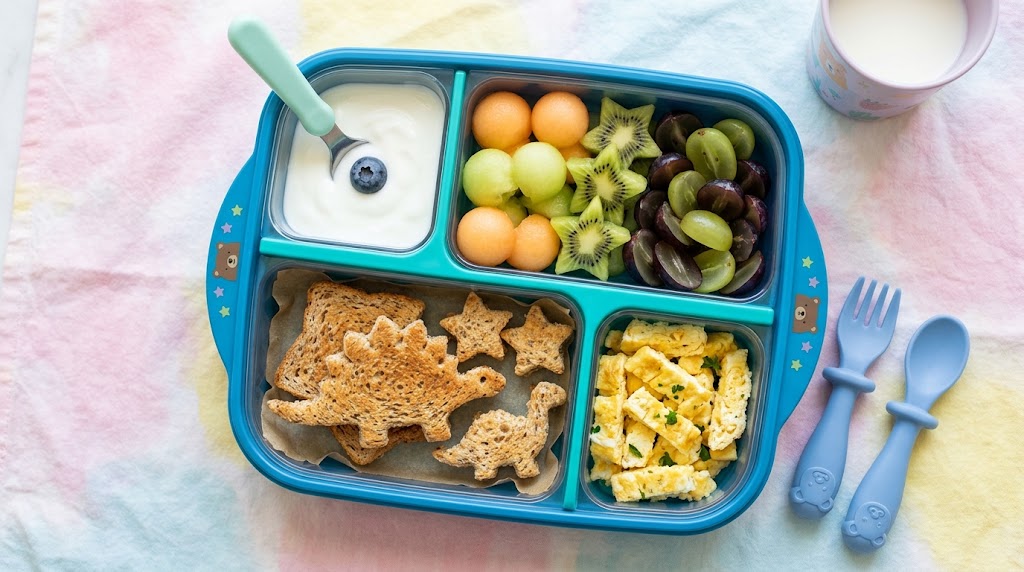 A colorful bento box breakfast with star-shaped fruit and dinosaur toast.