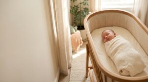 A peaceful newborn baby sleeping swaddled in a cradle in a softly-lit nursery, illustrating normal sleep